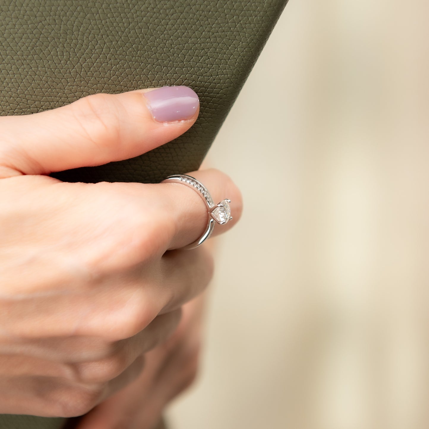 Close-up of a hand wearing a diamond ring on a neutral background