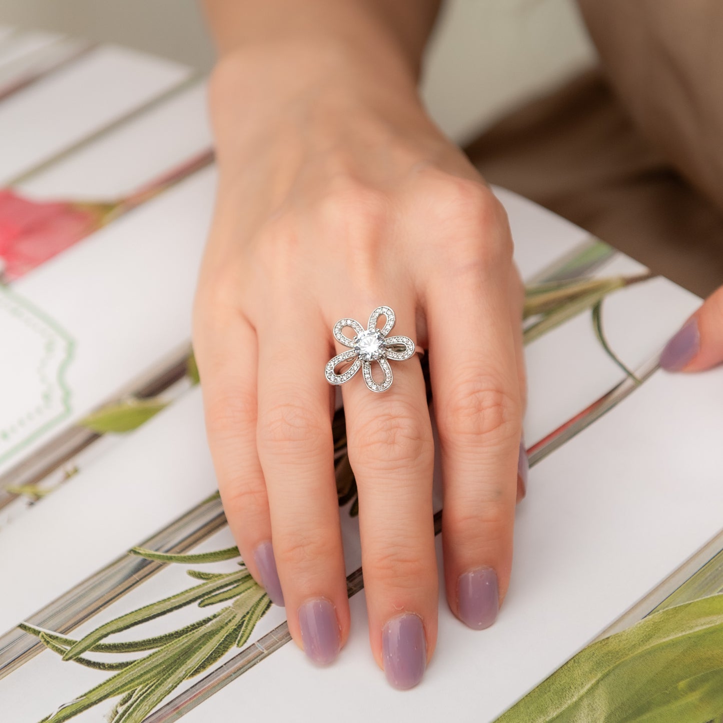 Hand wearing a silver ring with a floral design on a floral-patterned surface