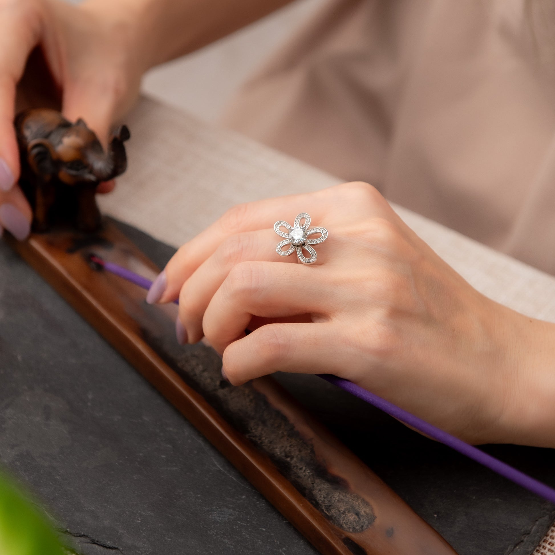 Person wearing a silver ring with a flower design on a stone surface.