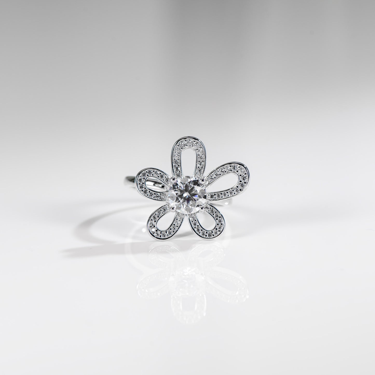 Silver flower-shaped ring with clear gemstone on a light gray background