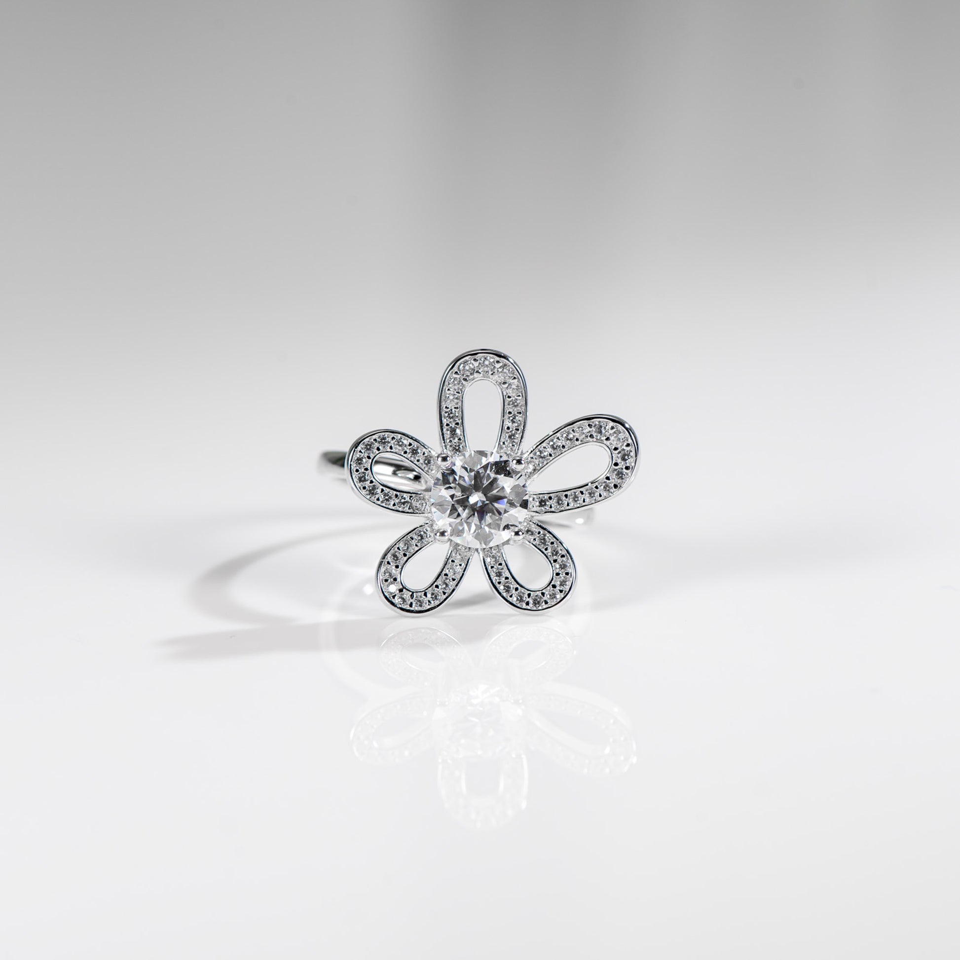 Silver flower-shaped ring with clear gemstone on a light gray background