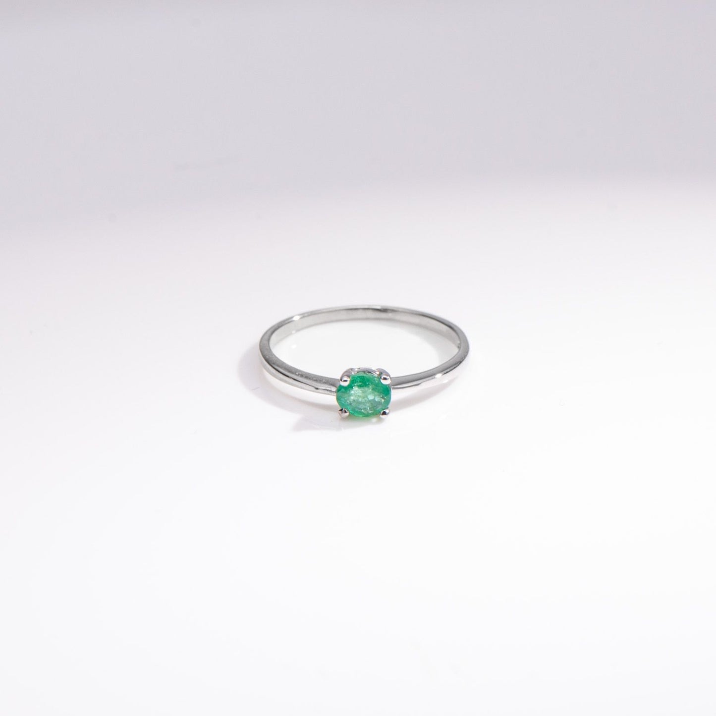 A silver ring with a small, round-cut green gemstone in a prong setting, photographed on a clean white background.