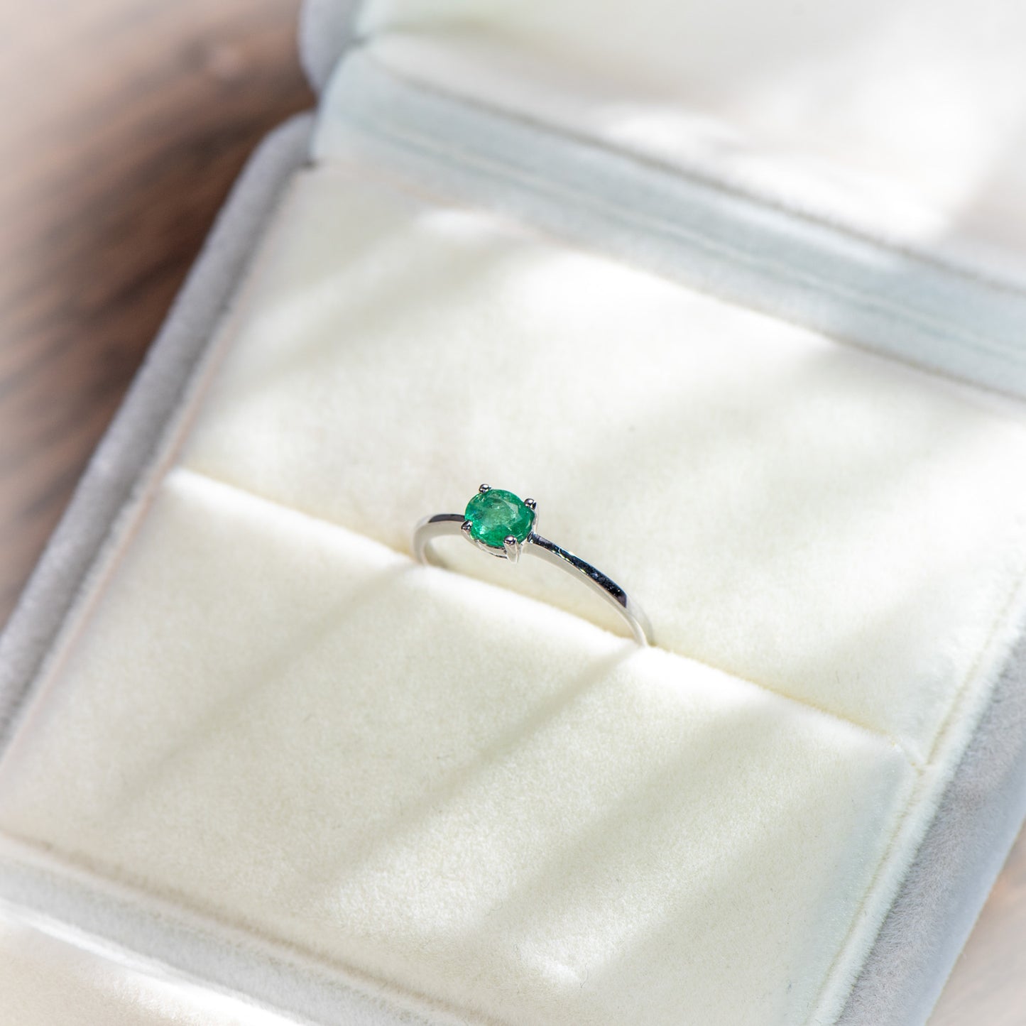 A silver ring with a square-cut green gemstone displayed inside an open white jewelry box.
