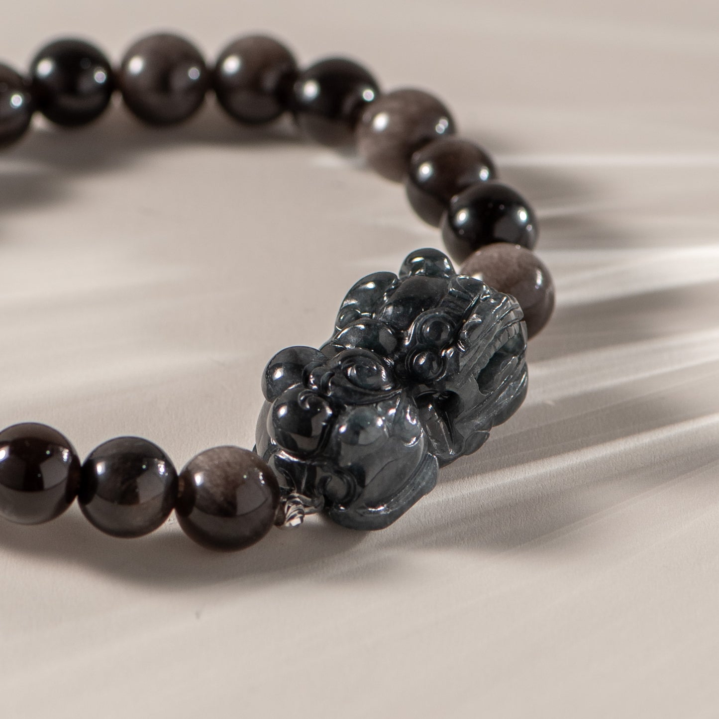 Black beaded bracelet with a central black stone pendant on a beige fabric background
