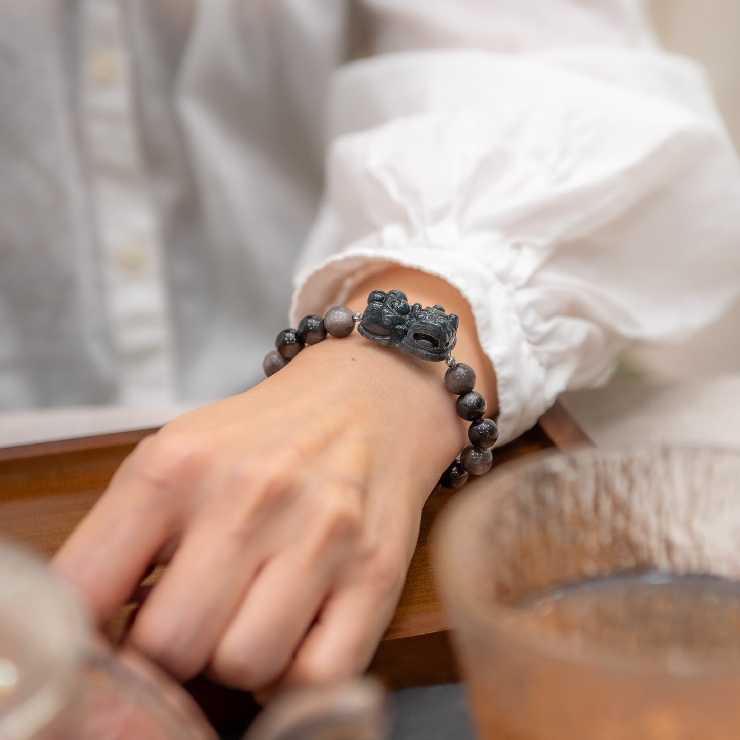 Person wearing a black beaded bracelet with a dragon design on a wooden surface.