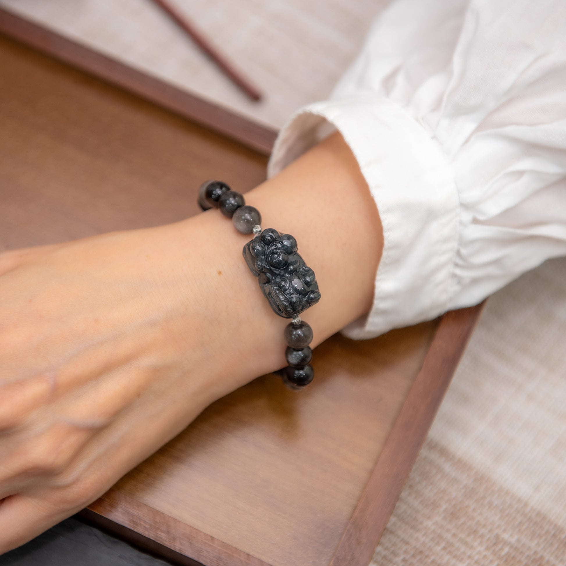 Person wearing a black beaded bracelet on a wooden surface