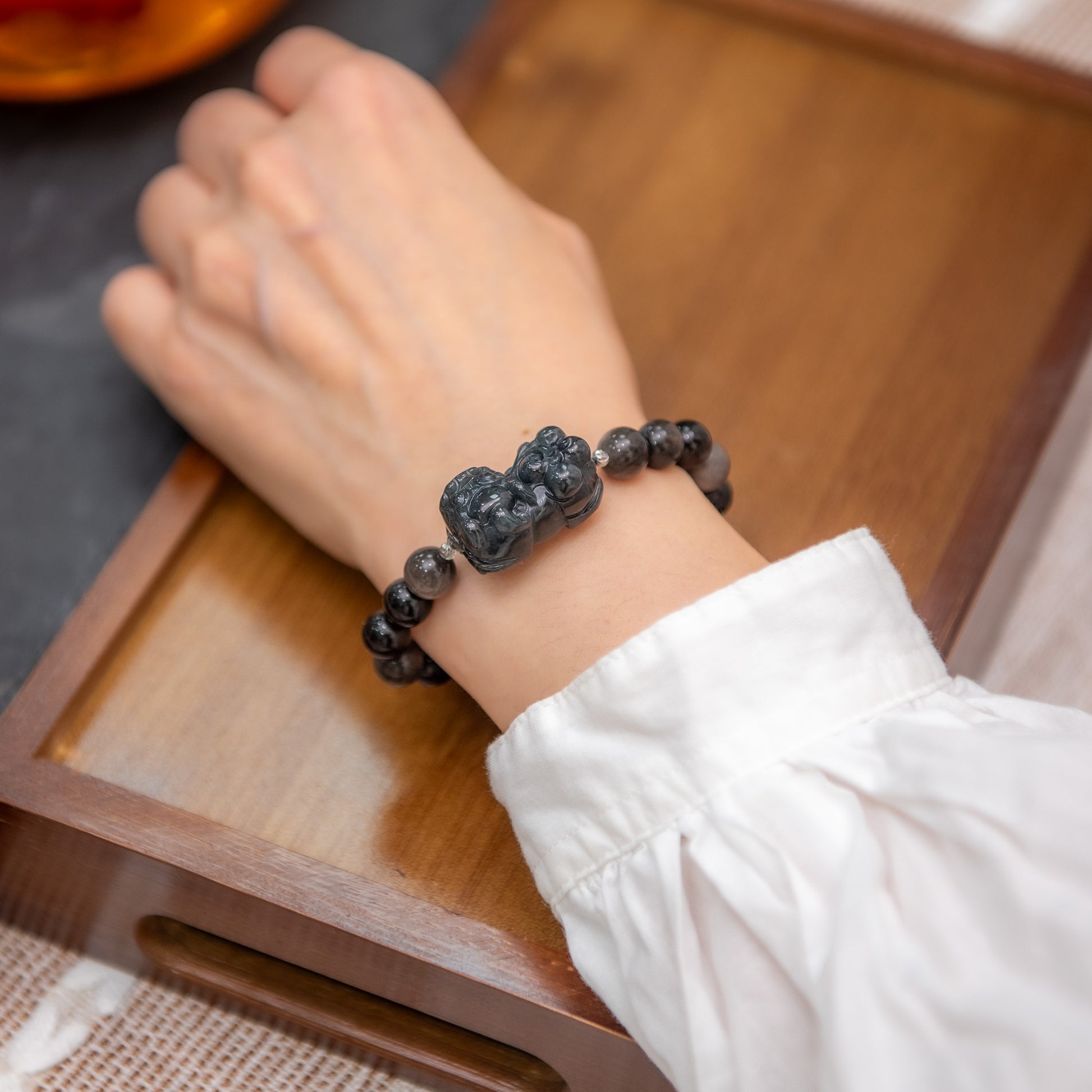 Person wearing a black beaded bracelet on a wooden surface