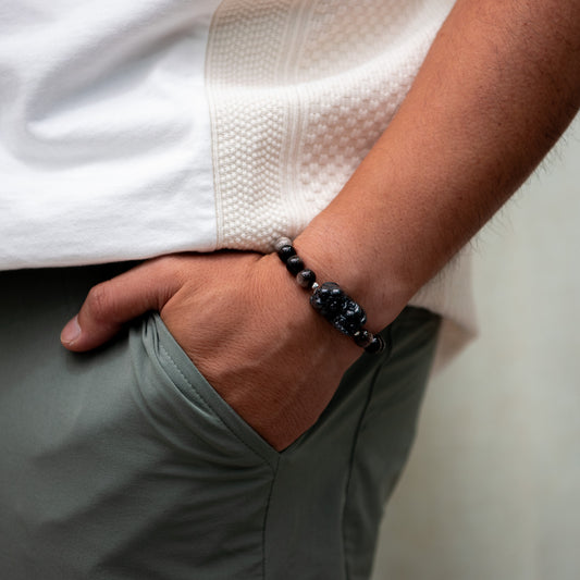 Person wearing a black beaded bracelet on a neutral background