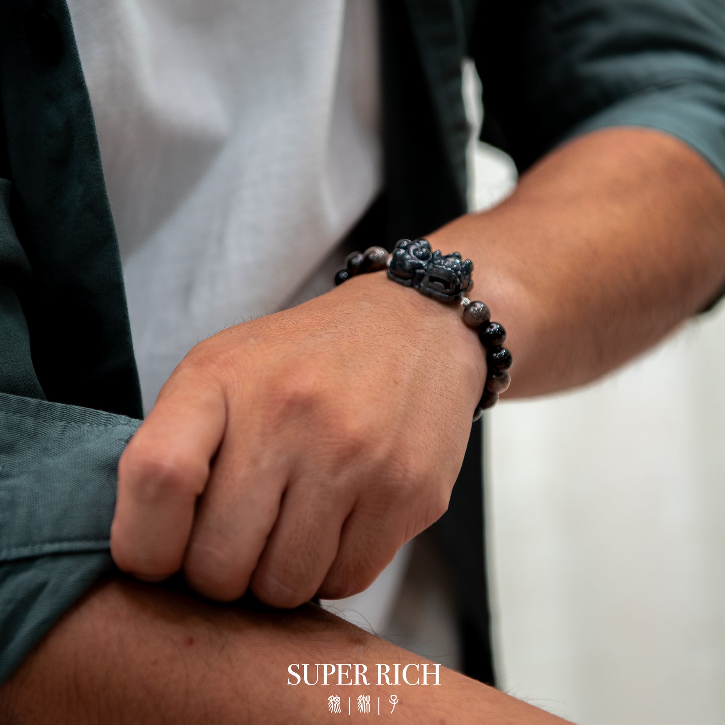 Person wearing a bracelet with 'SUPER RICH' branding on a blurred background