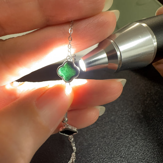 Hand holding a clover-shaped pendant with a green gemstone under a flashlight.
