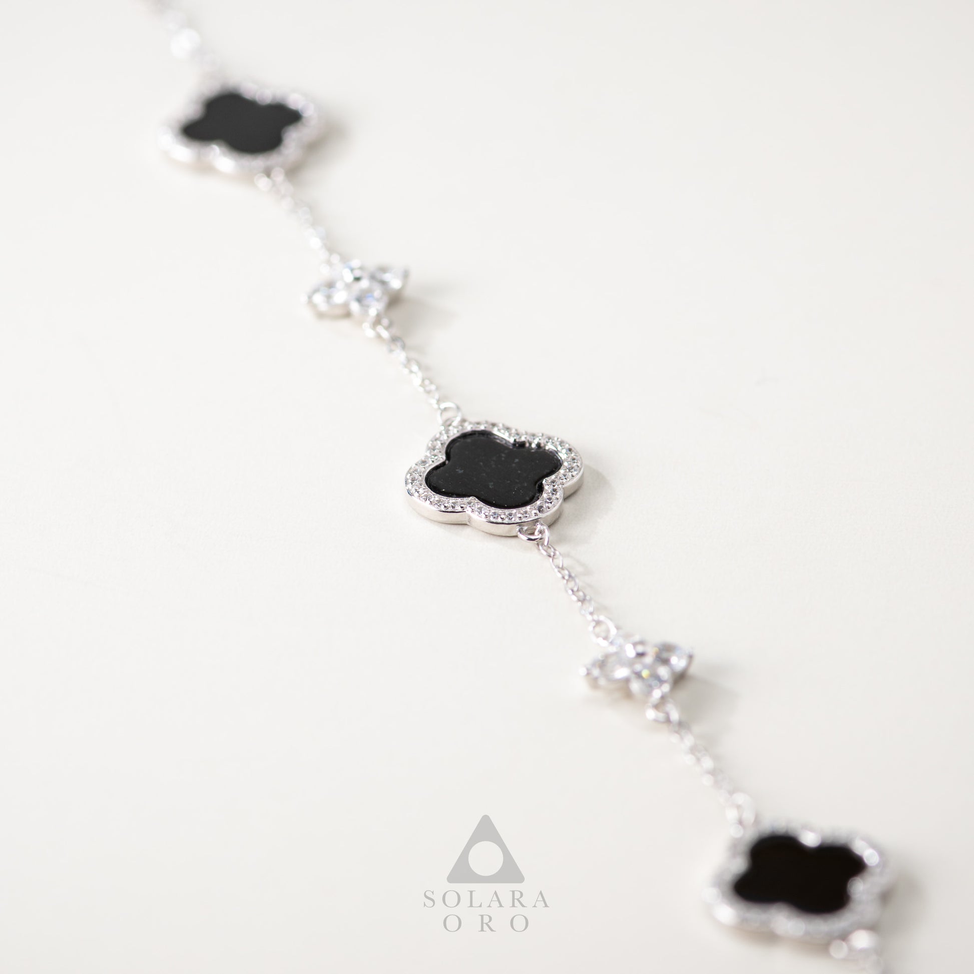 Silver necklace with black clover-shaped pendants on a white background, featuring the Solara Oro brand.