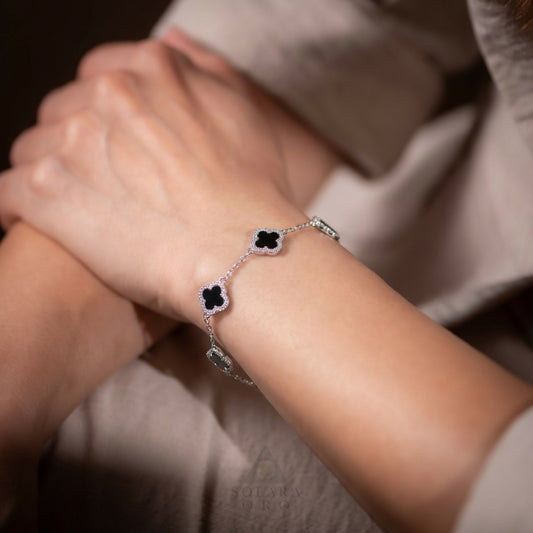 Close-up of a wrist wearing a delicate bracelet with black clover-shaped charms.