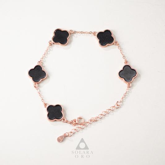 Rose gold bracelet with black clover-shaped charms on a white background, featuring the Solara Oro brand.