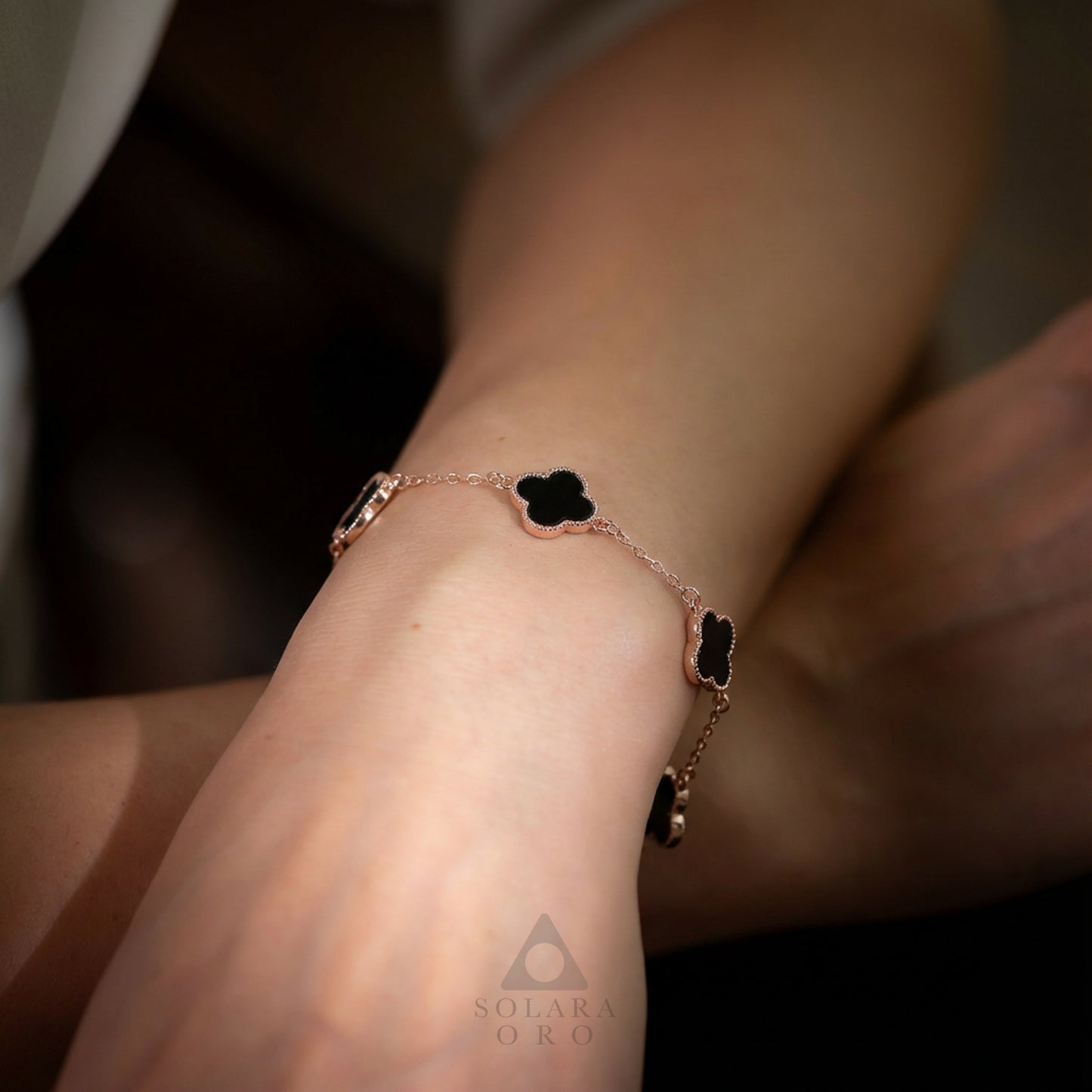 Rose gold bracelet with black heart charms on a wrist, brand 'Solara Oro' visible.