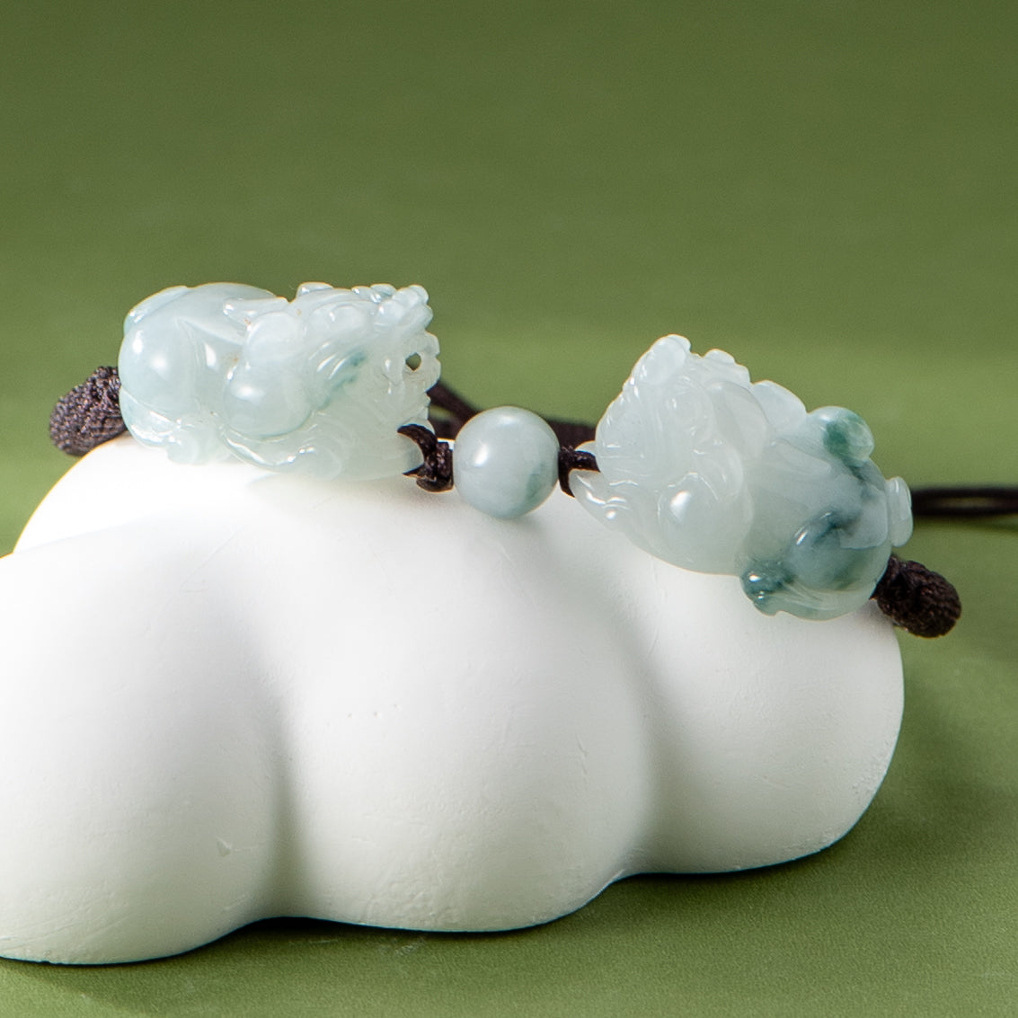 Jade bracelet with pixic designs on a white cloud-shaped base against a green background.