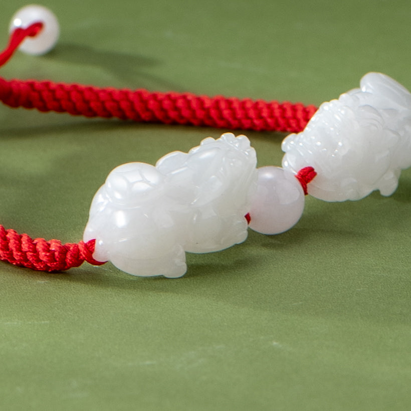 White carved animal beads on a red cord against a green background