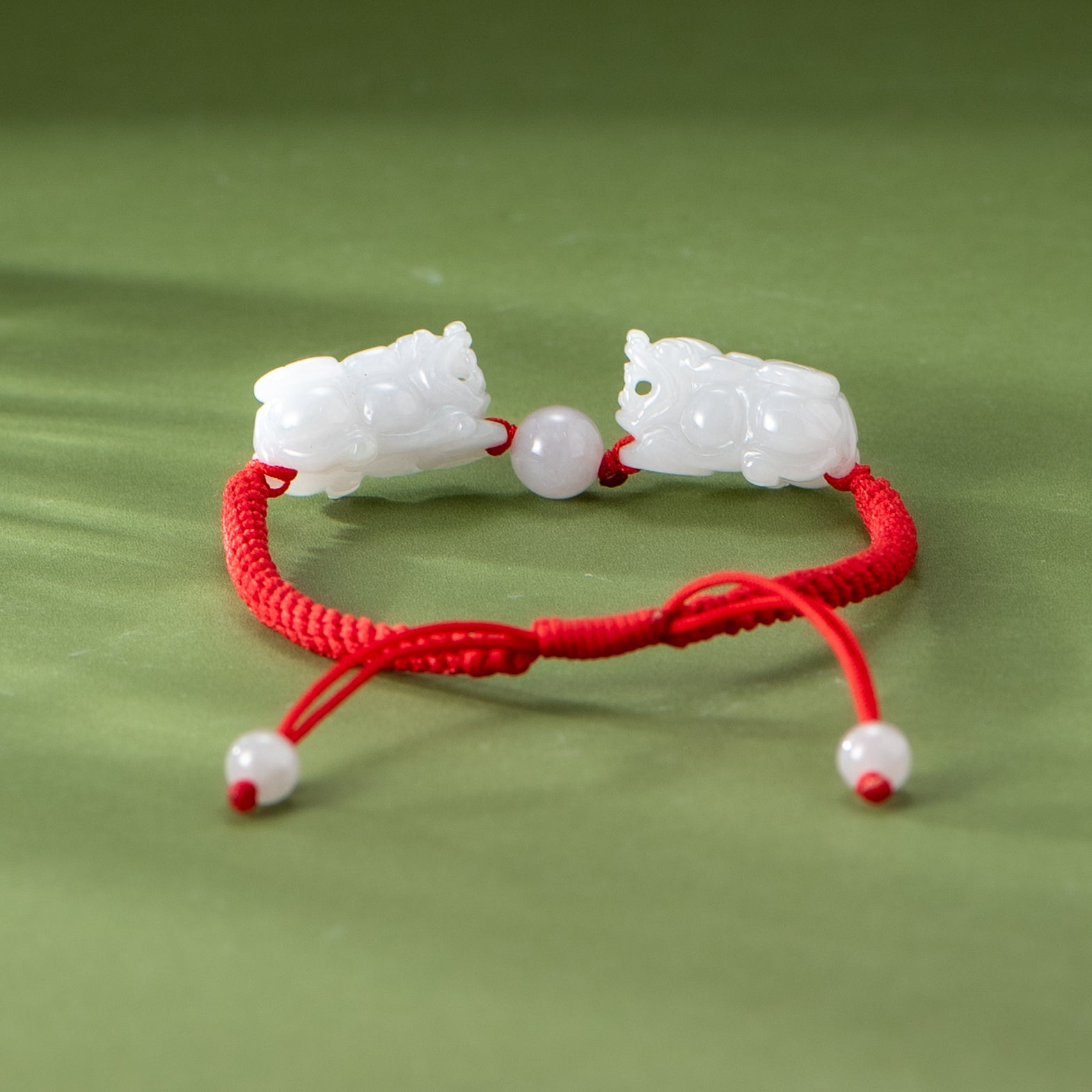 Bracelet with white stone lions and red cord on a green background