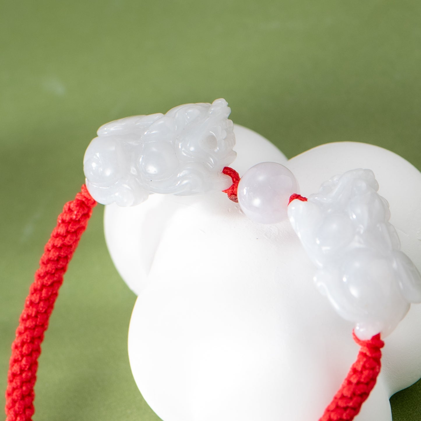 White jade pendant with red cord on a green background