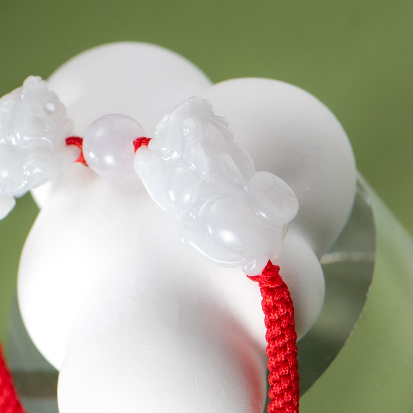 Close-up of a white jade pendant with a red string on a green background