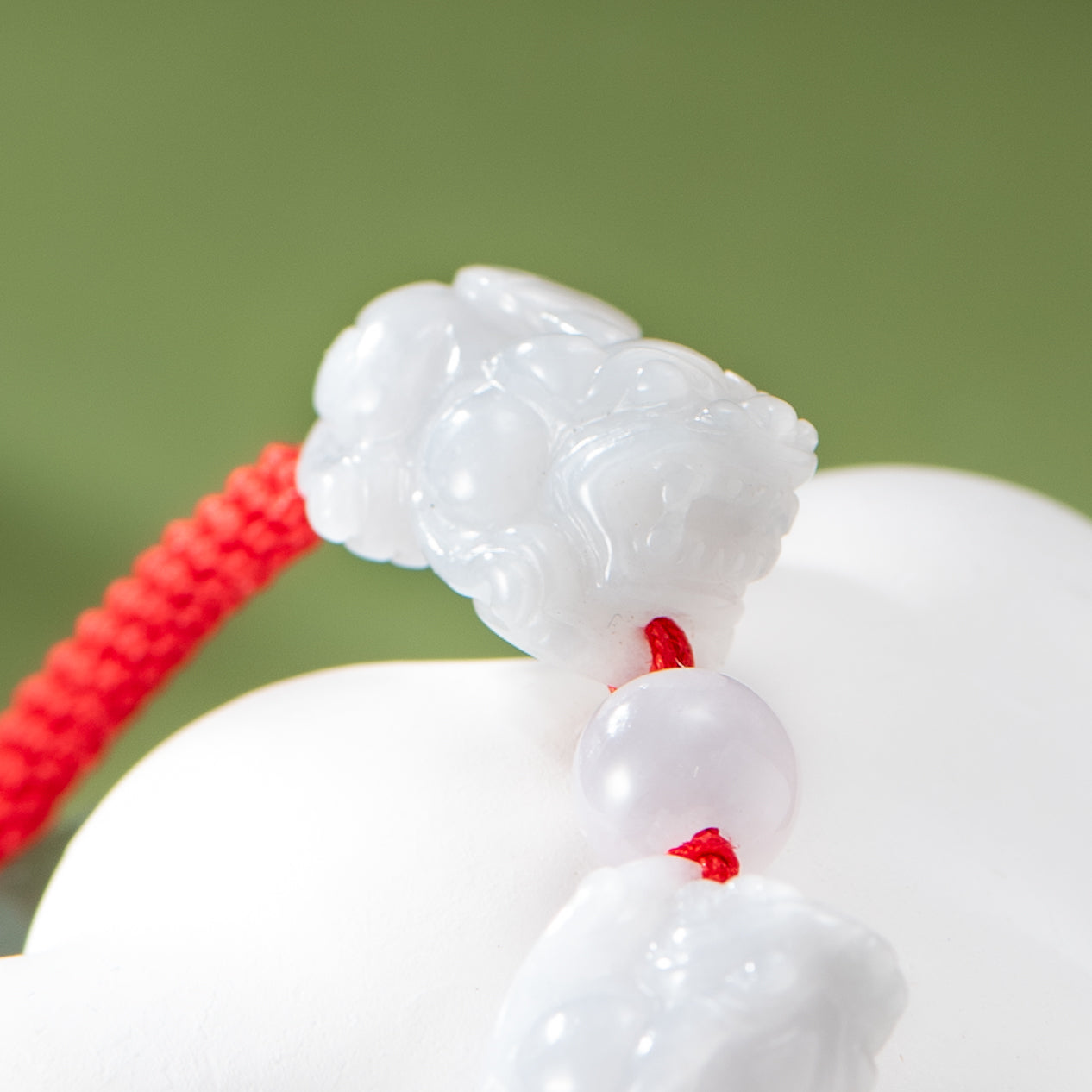 White jade pendant with red string on a green background