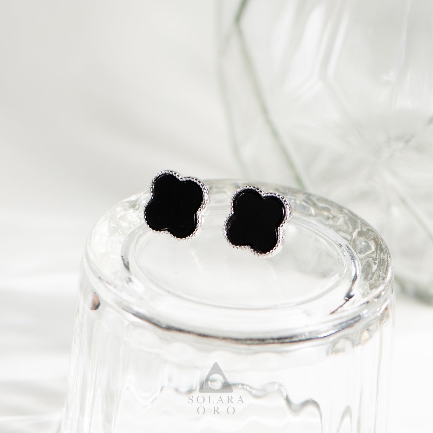 Black flower-shaped earrings on a glass jar with 'Solerara Oro' branding.