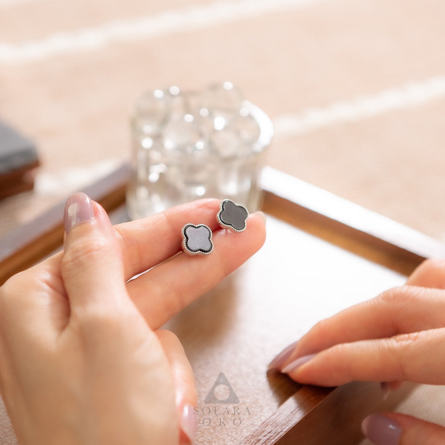 Clover-shaped earrings held between fingers with a blurred background