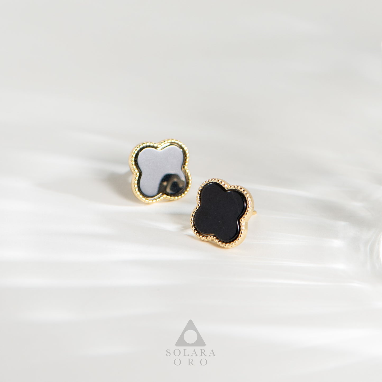 Pair of gold earrings with black and white clover-shaped stones on a white background.