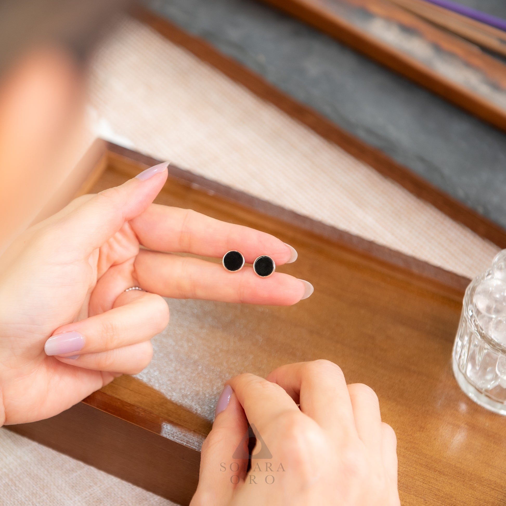 Person holding two black earrings on a wooden surface