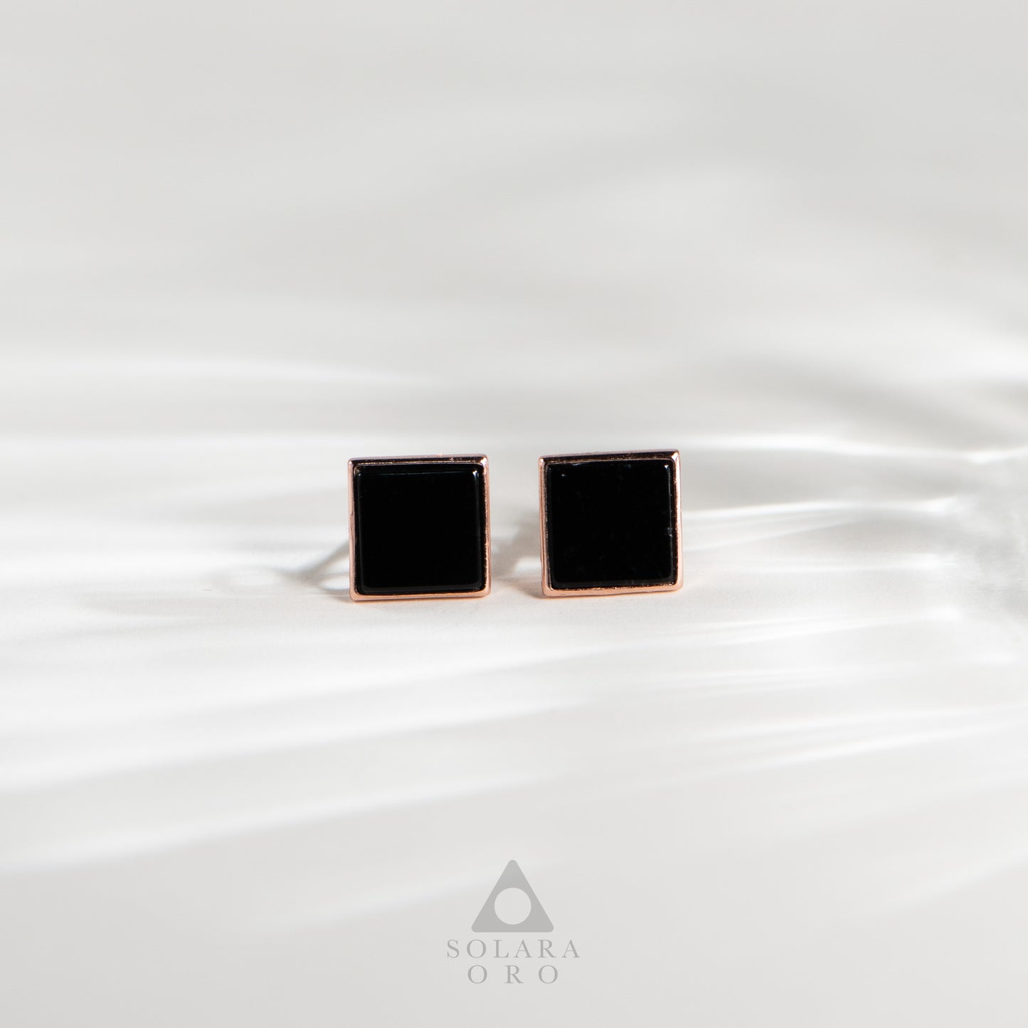 Black square cufflinks with rose gold border on white satin background