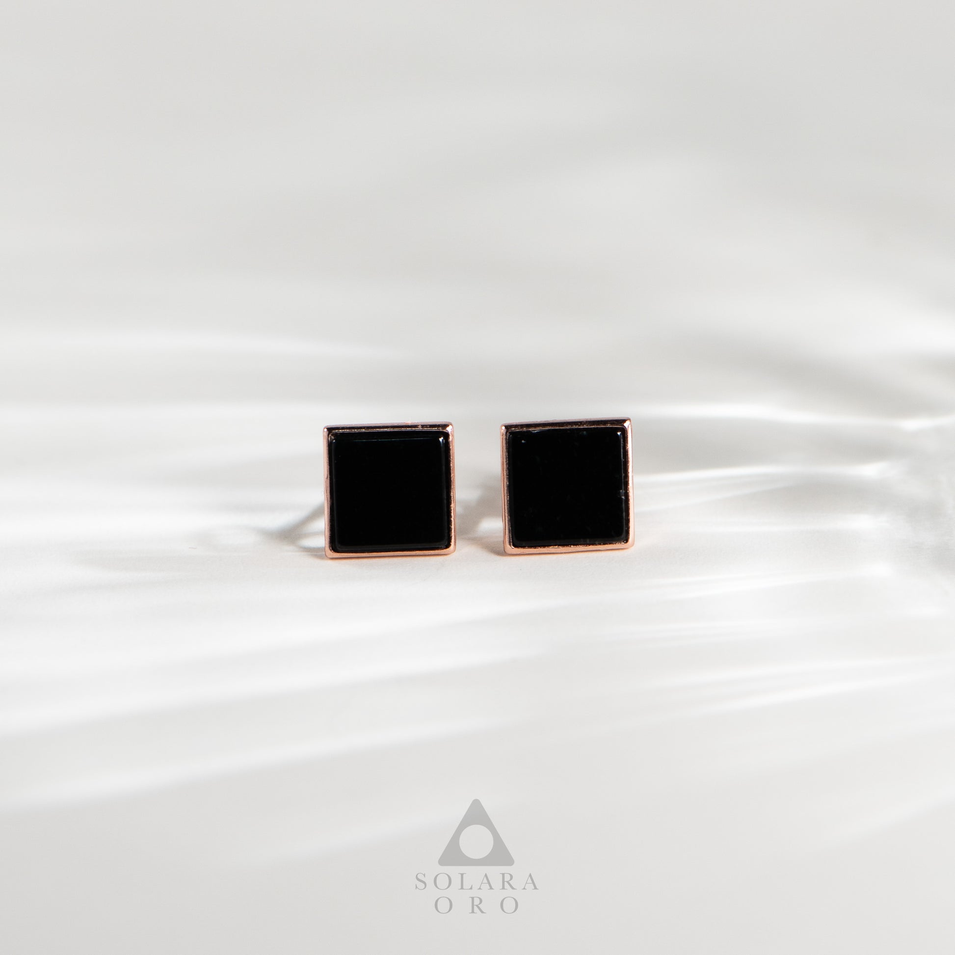 Black square cufflinks with rose gold border on white satin background