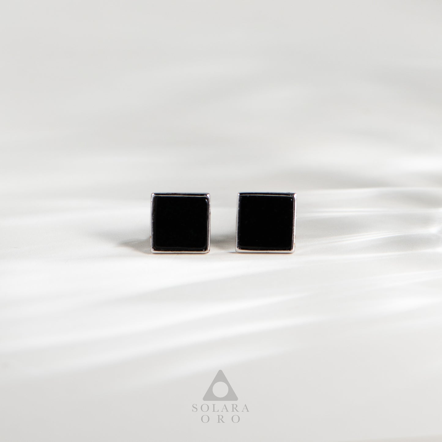 Black square cufflinks on a white satin background with Solara Oro logo.
