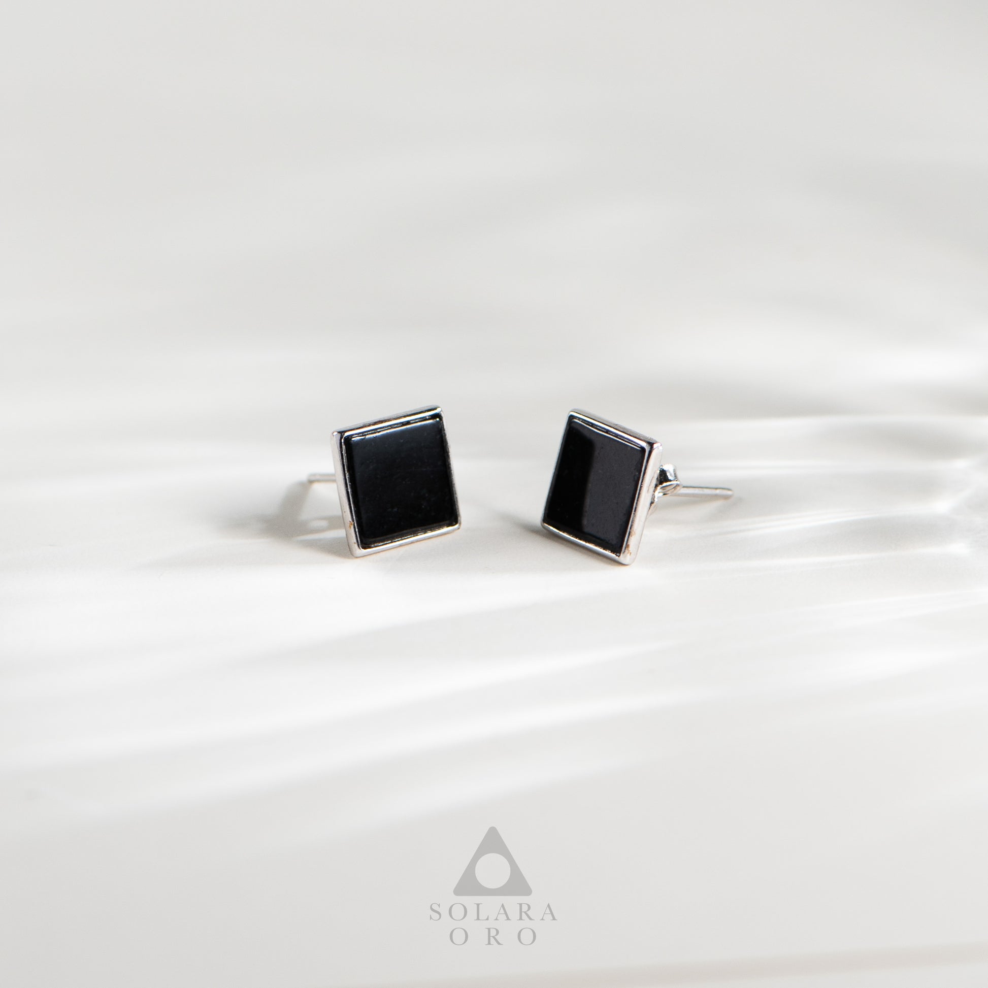 Square black cufflinks on a white satin background with Solara Oro logo.