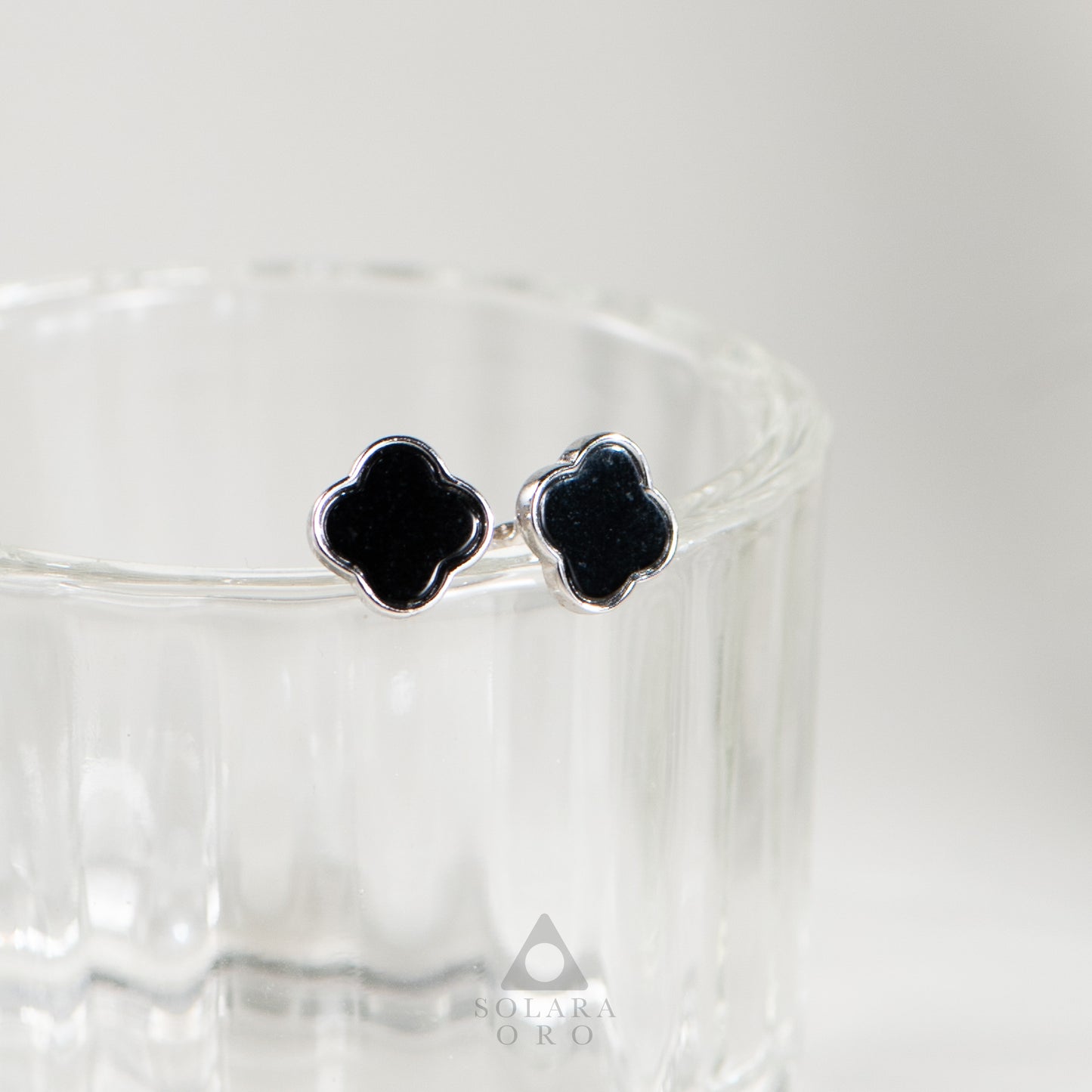 Black clover-shaped earrings on a clear stand with a white background