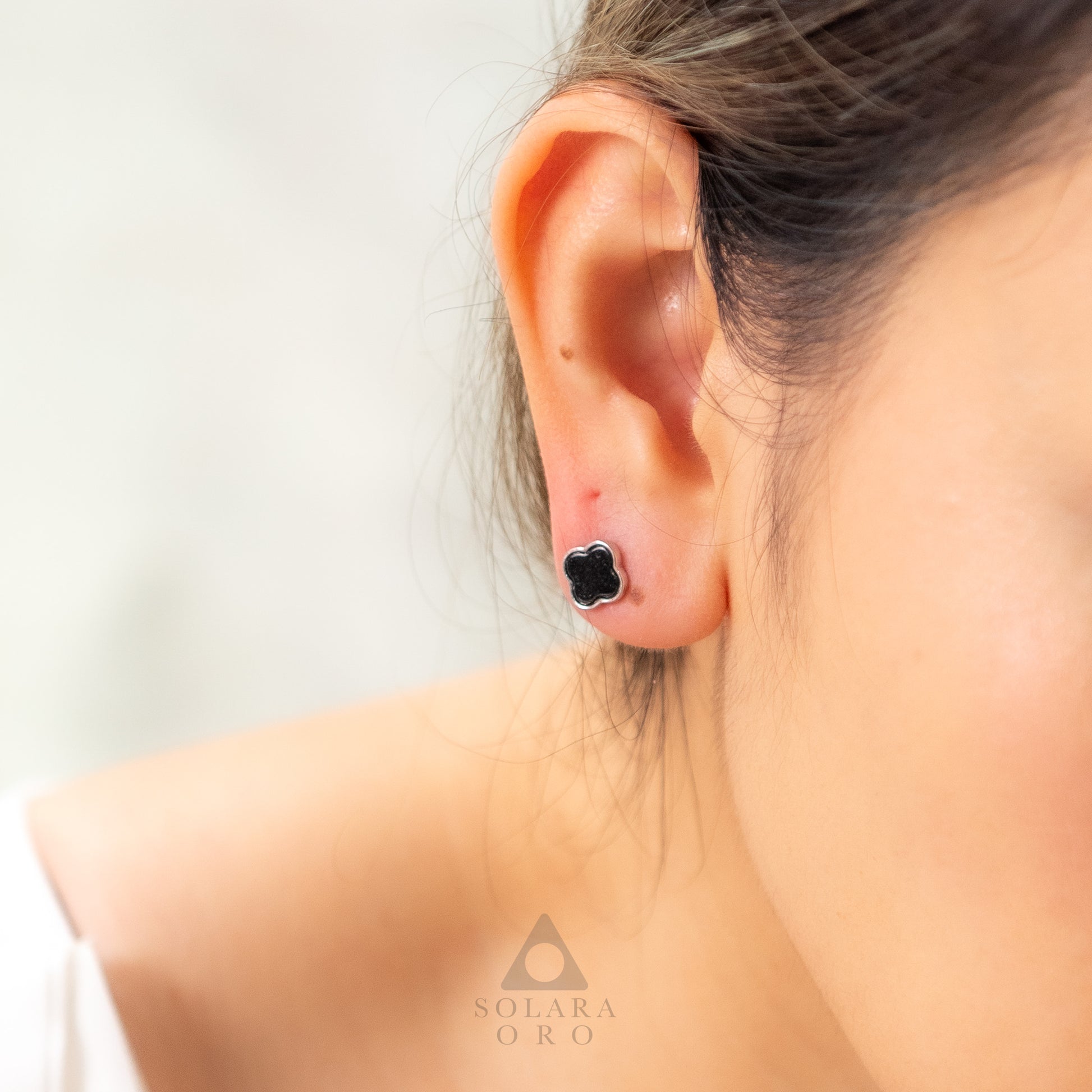Close-up of an ear wearing a black clover-shaped earring with a blurred background