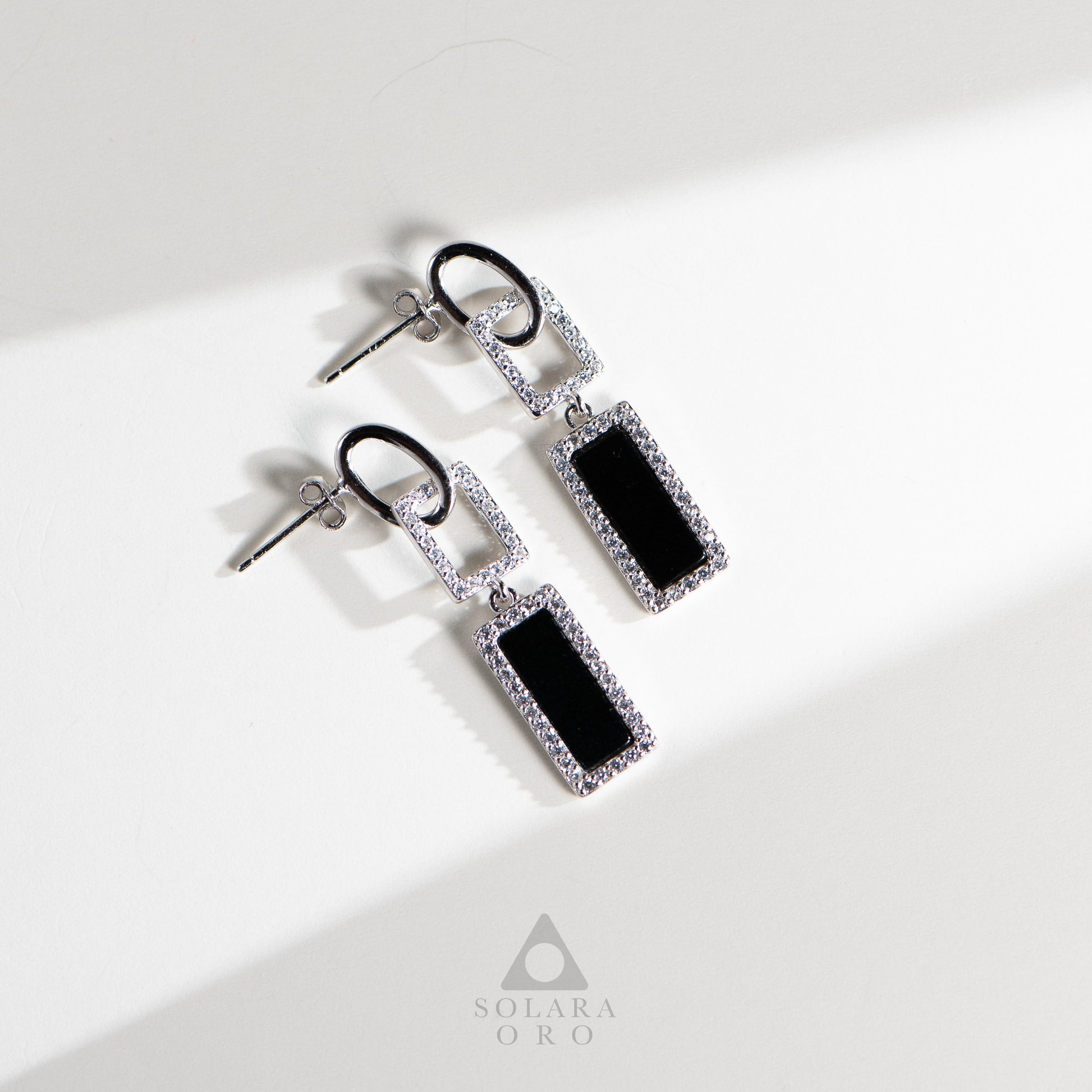 Pair of earrings with black rectangular stones and silver accents on a white background, branded 'Soleara Oro'.