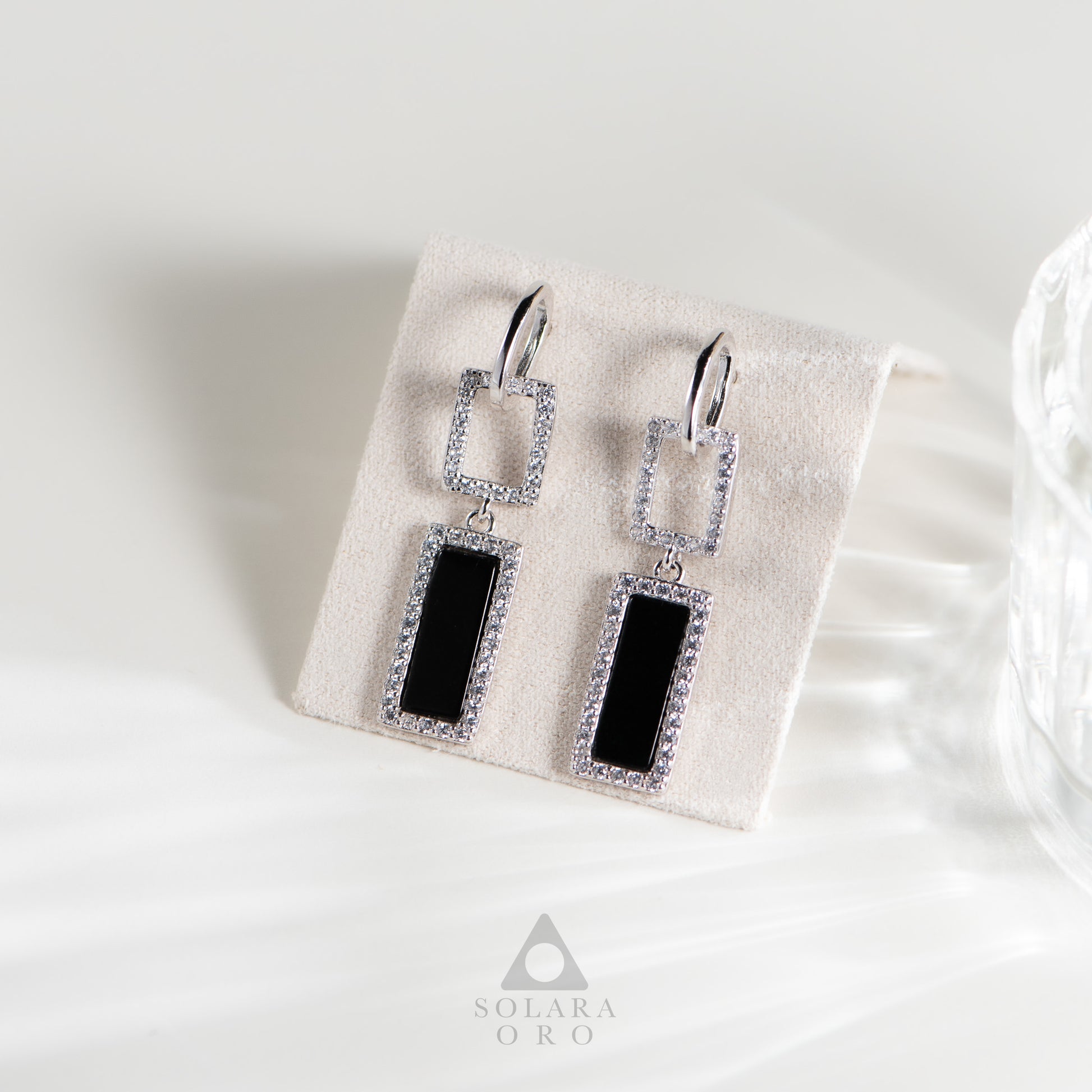 Pair of earrings with black stones on a white background, featuring the Solara Oro brand.