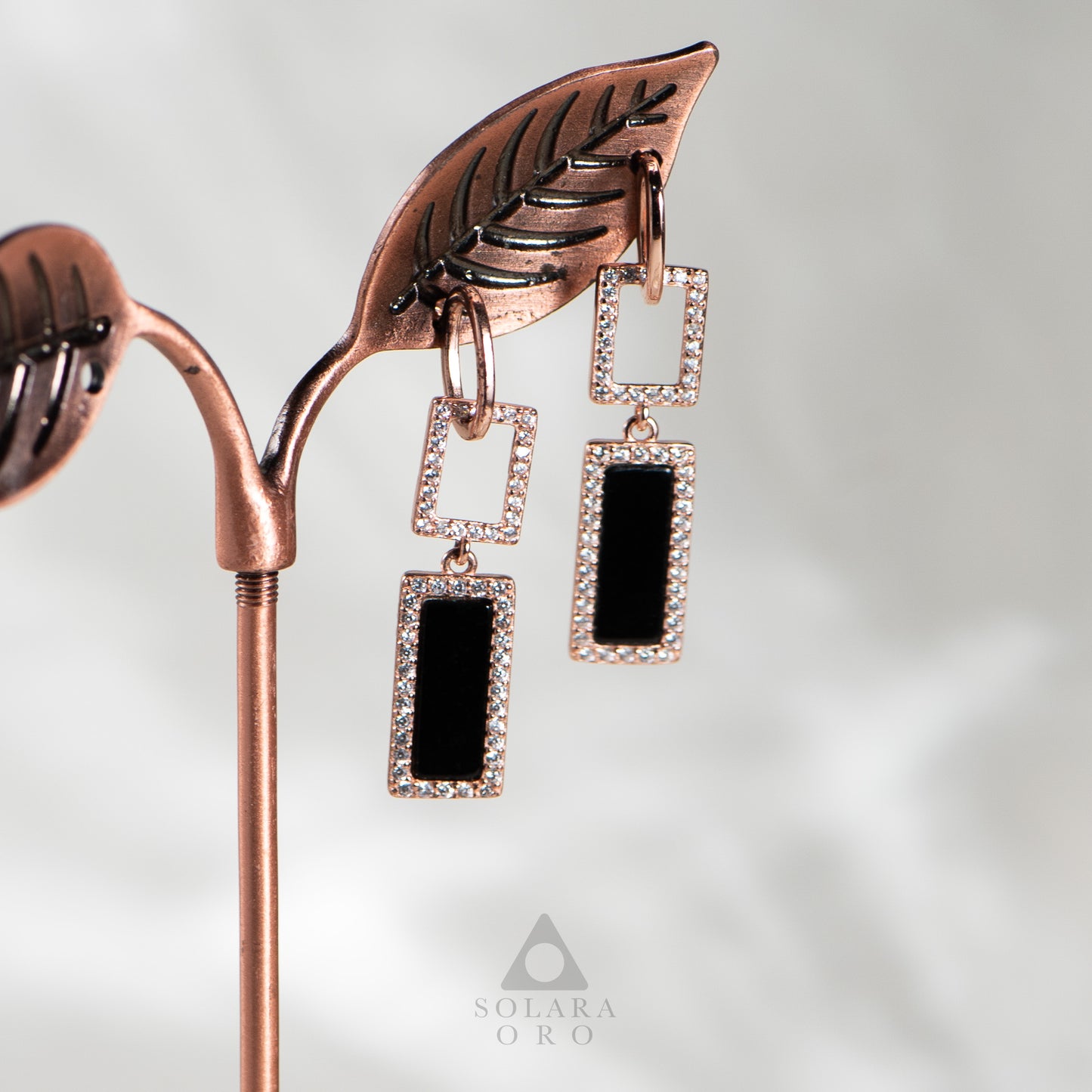 Rose gold earrings with black stones on a white background, featuring the Solara Oro brand.