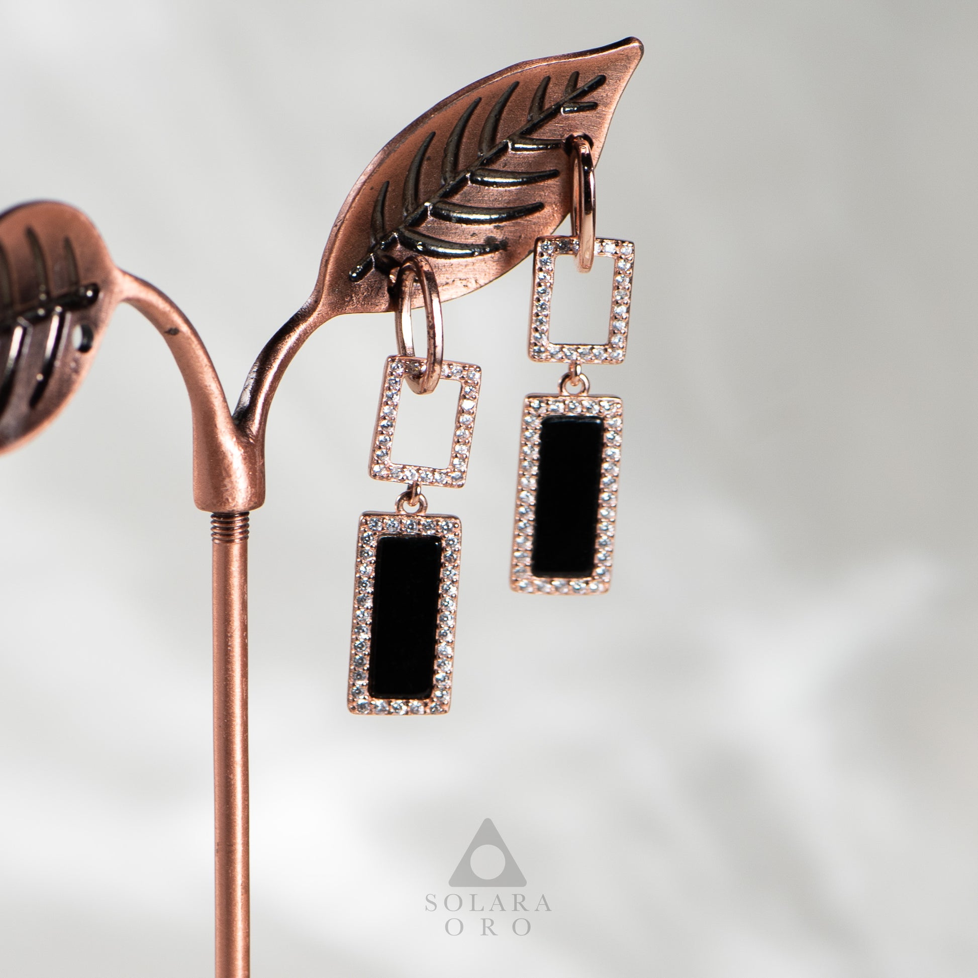 Rose gold earrings with black stones on a white background, featuring the Solara Oro brand.