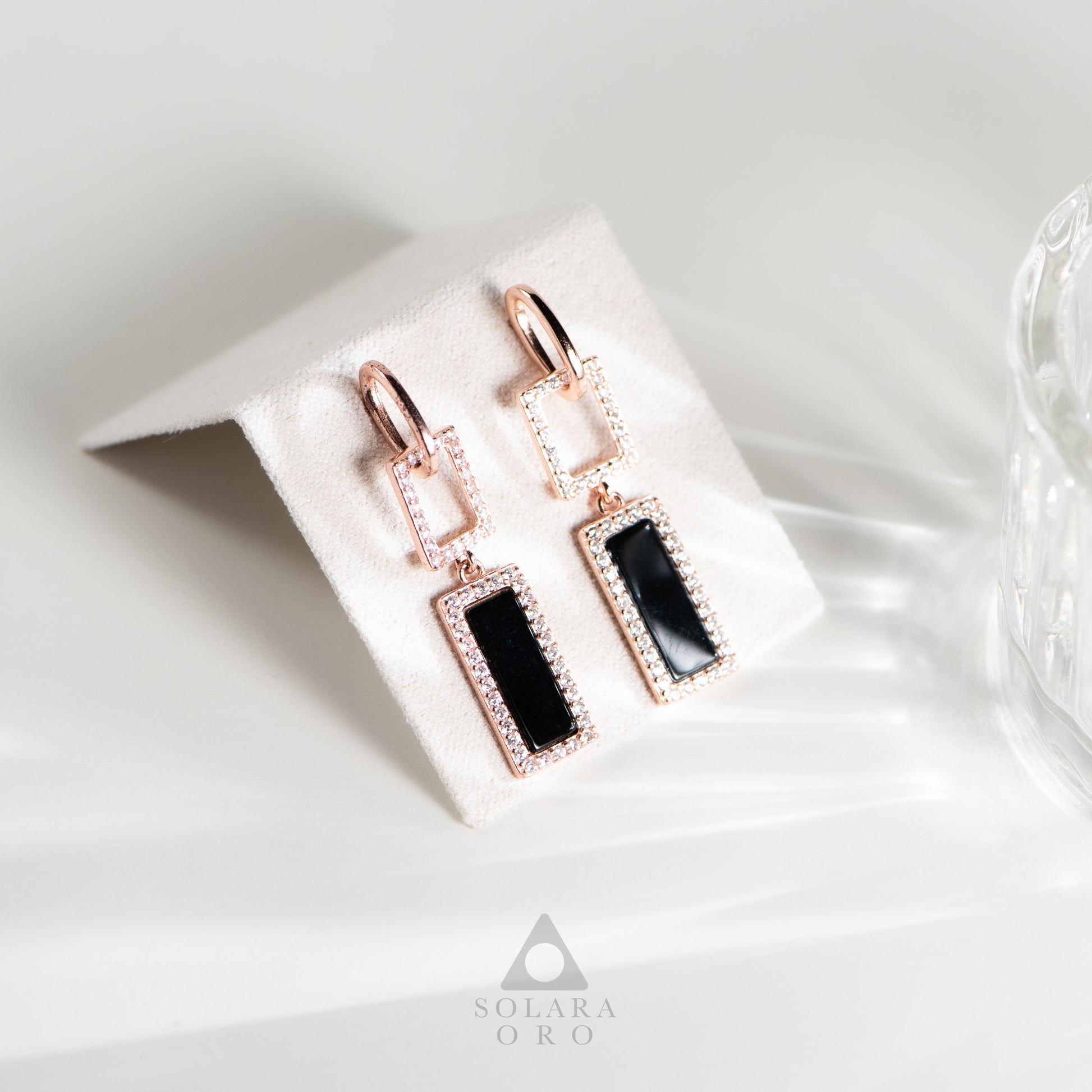 Rose gold earrings with black stones on a white card, branded 'Soleara Oro'.