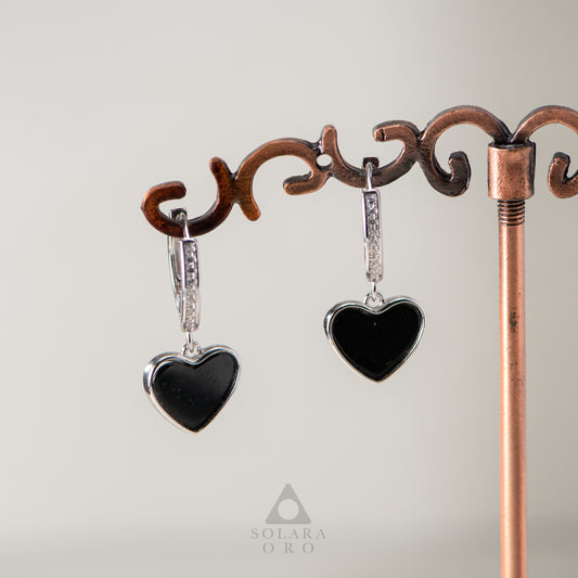 Heart-shaped earrings with black stones on a decorative stand, featuring the brand 'Soleara Oro'.
