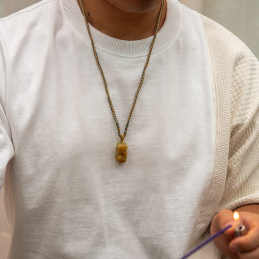 Person wearing a white shirt with a necklace, holding a lit candle.