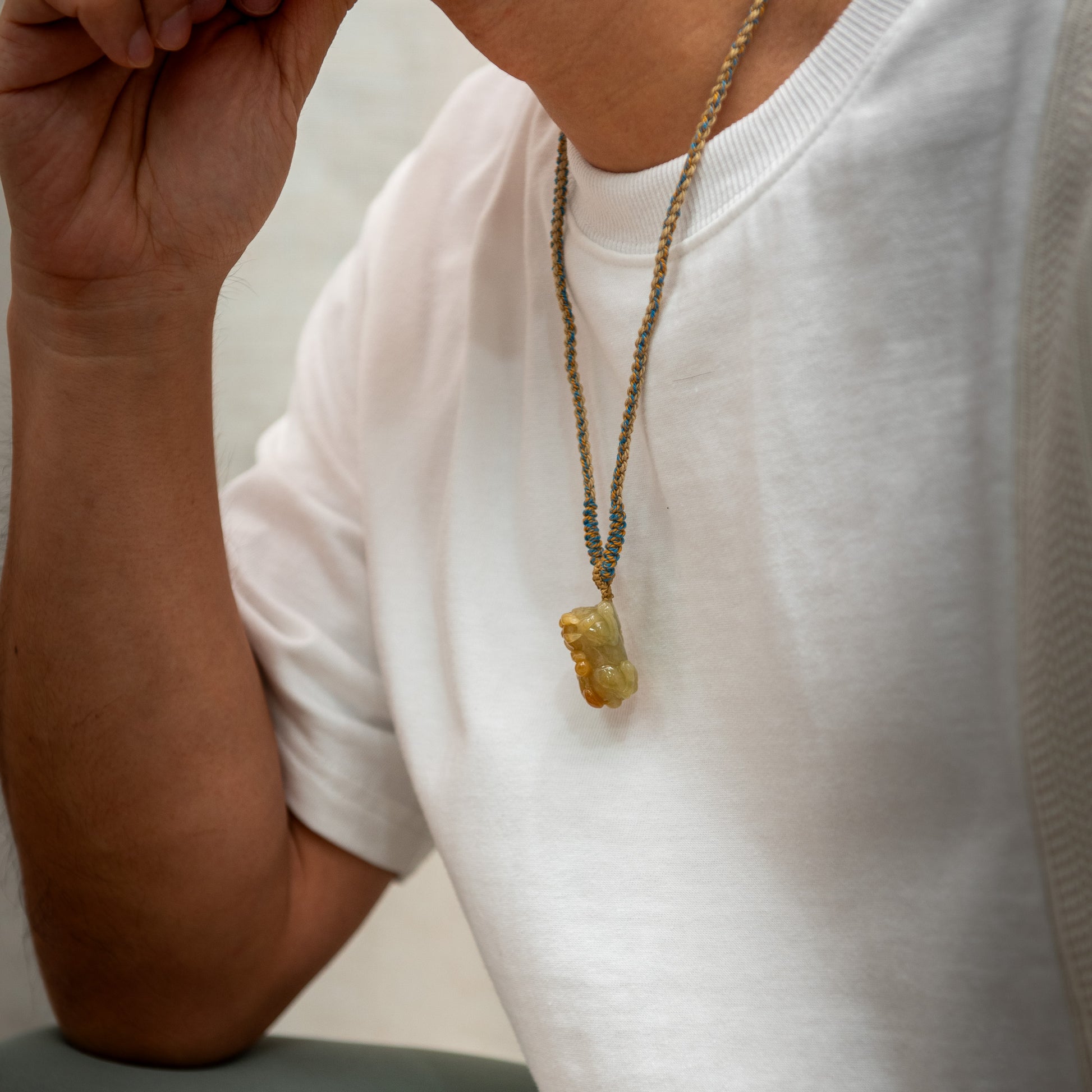 Person wearing a white shirt with a necklace featuring a green stone pendant.