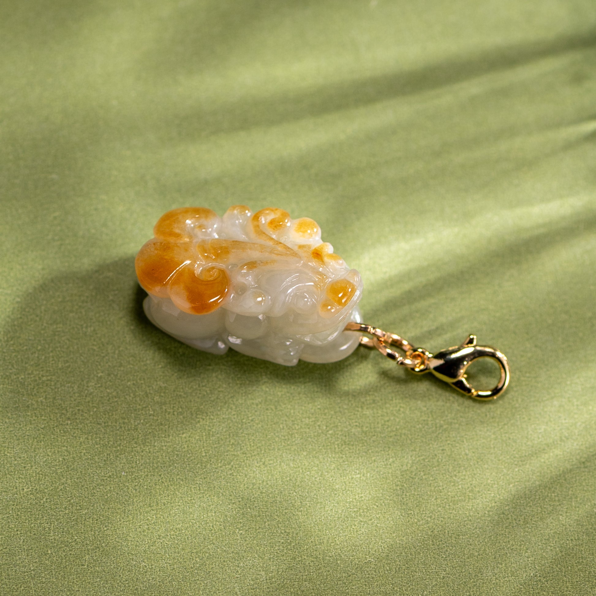 Carved stone pendant with gold chain on a green fabric background