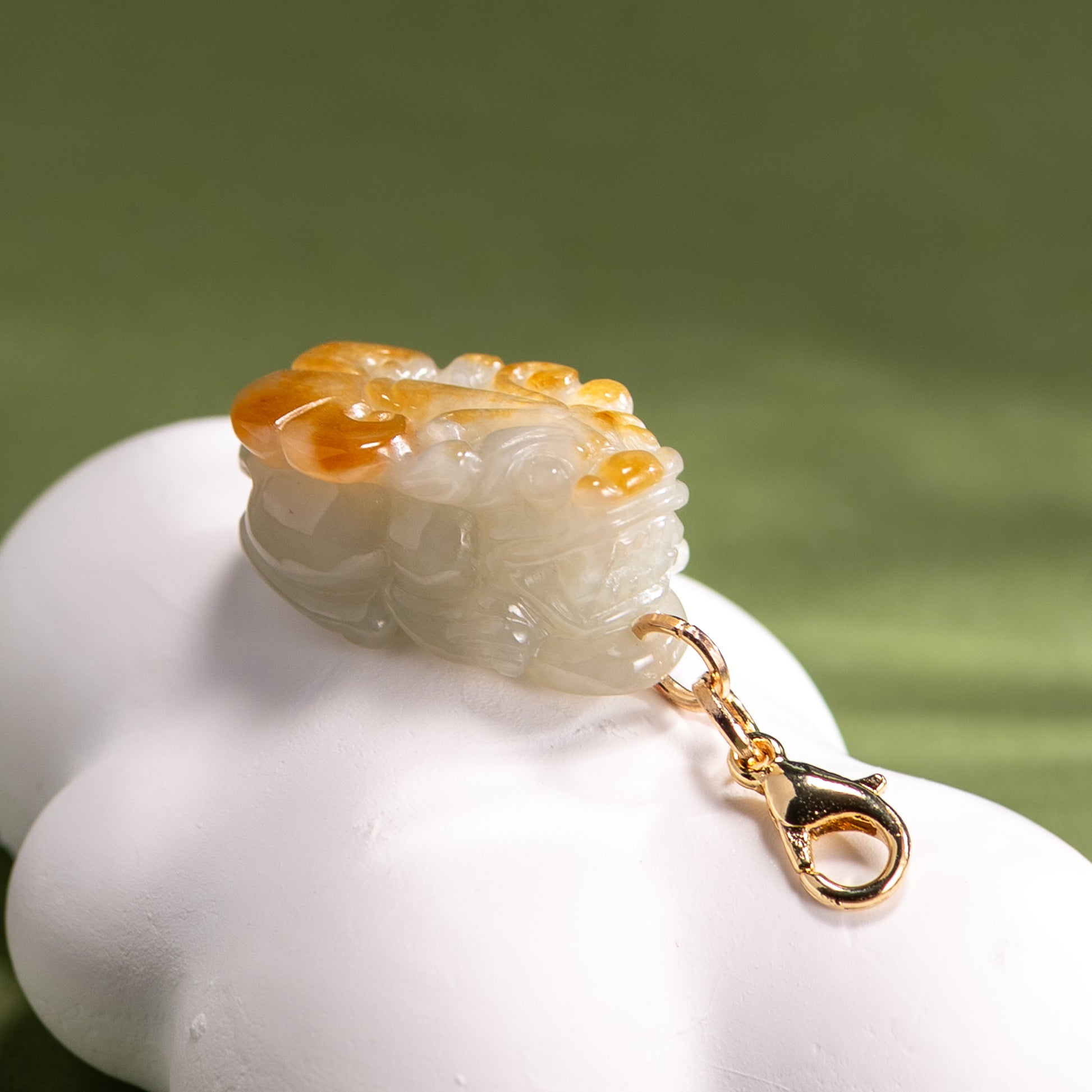 Carved jade pendant with gold chain on a white base against a green background