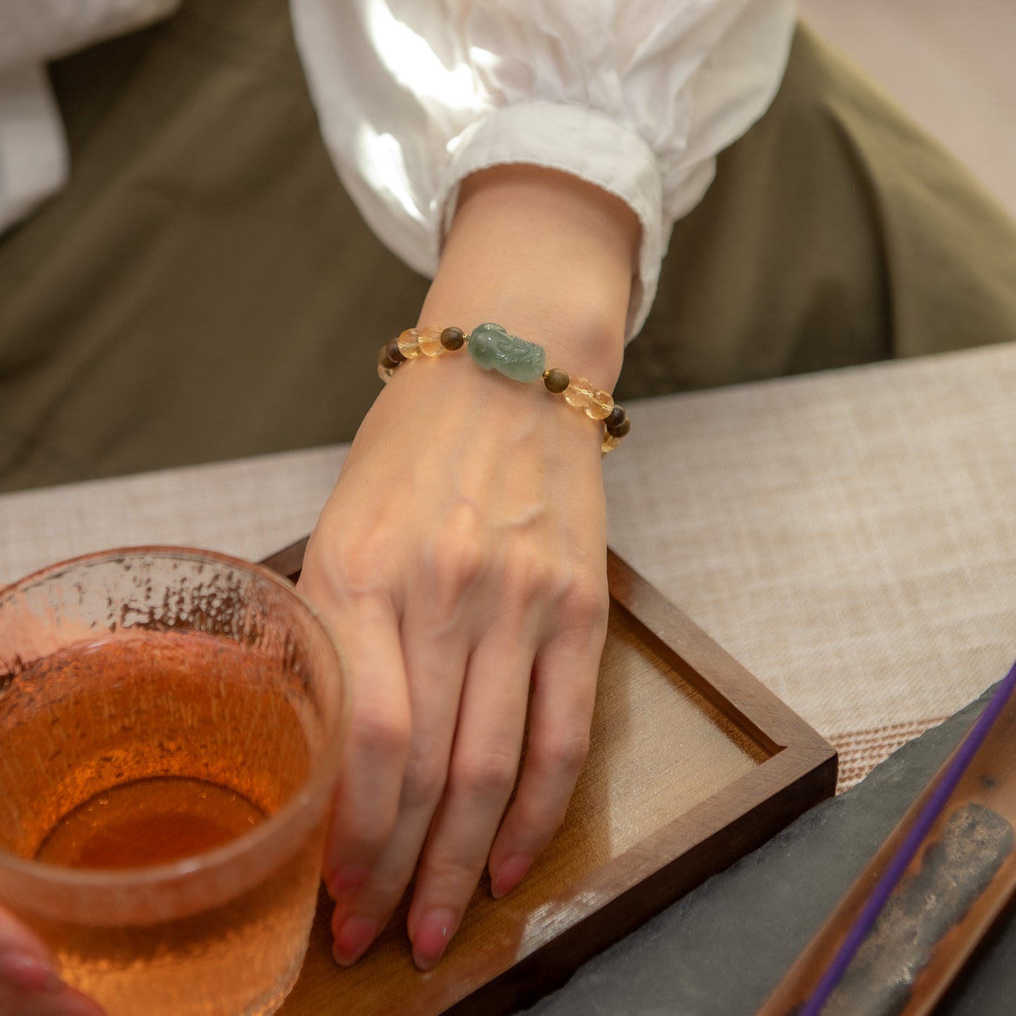 Hand wearing a bracelet with a glass of tea on a wooden tray