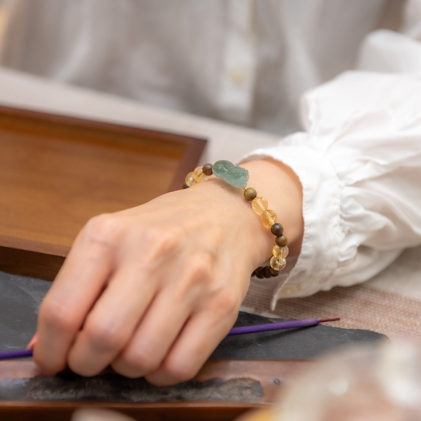 Person wearing a beaded bracelet on a table with a blurred background