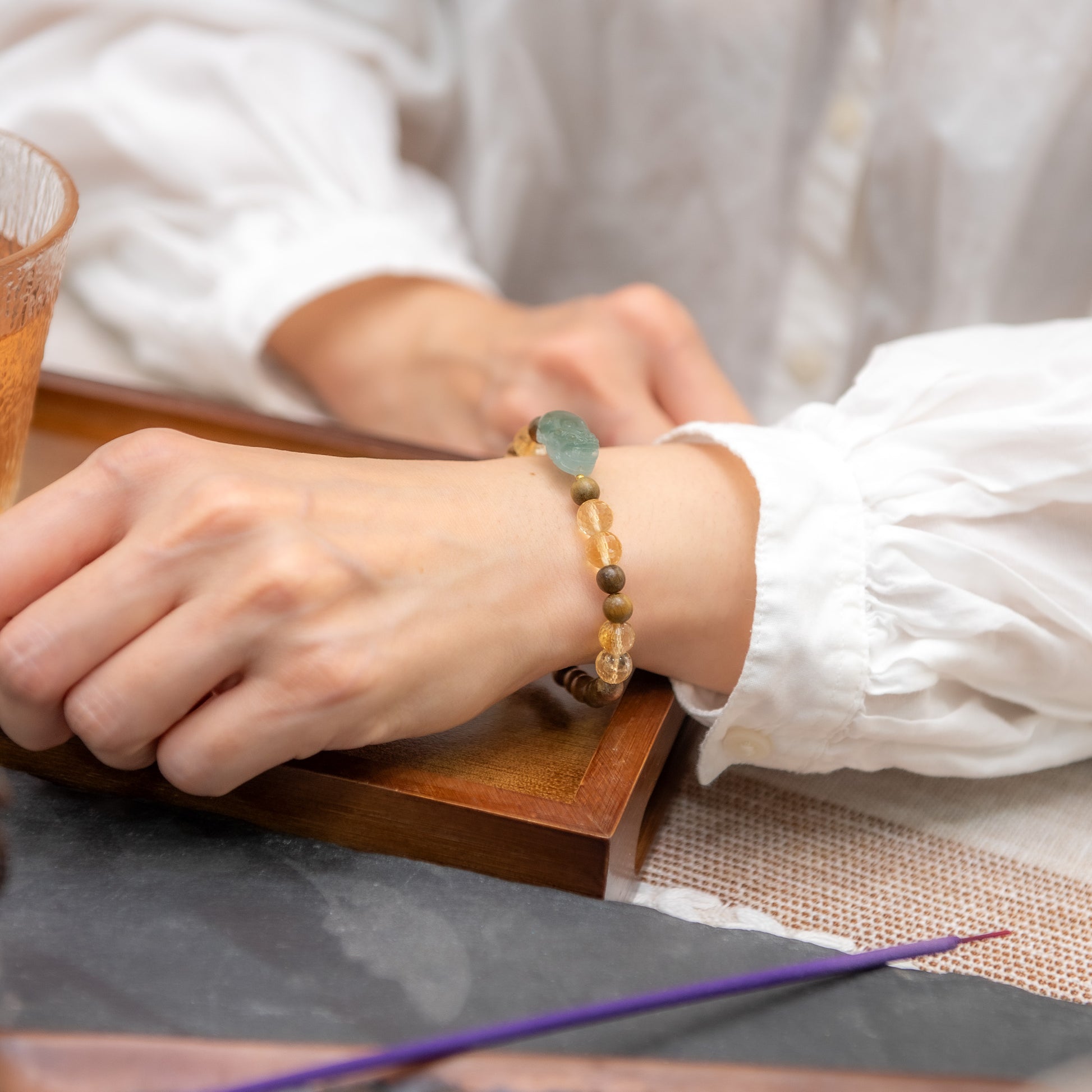 Person wearing a beaded bracelet on a table with a glass of tea and a purple straw.
