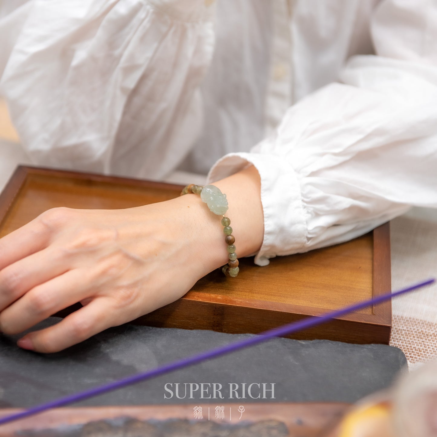 Person wearing a bracelet with a wooden box and purple object in the foreground