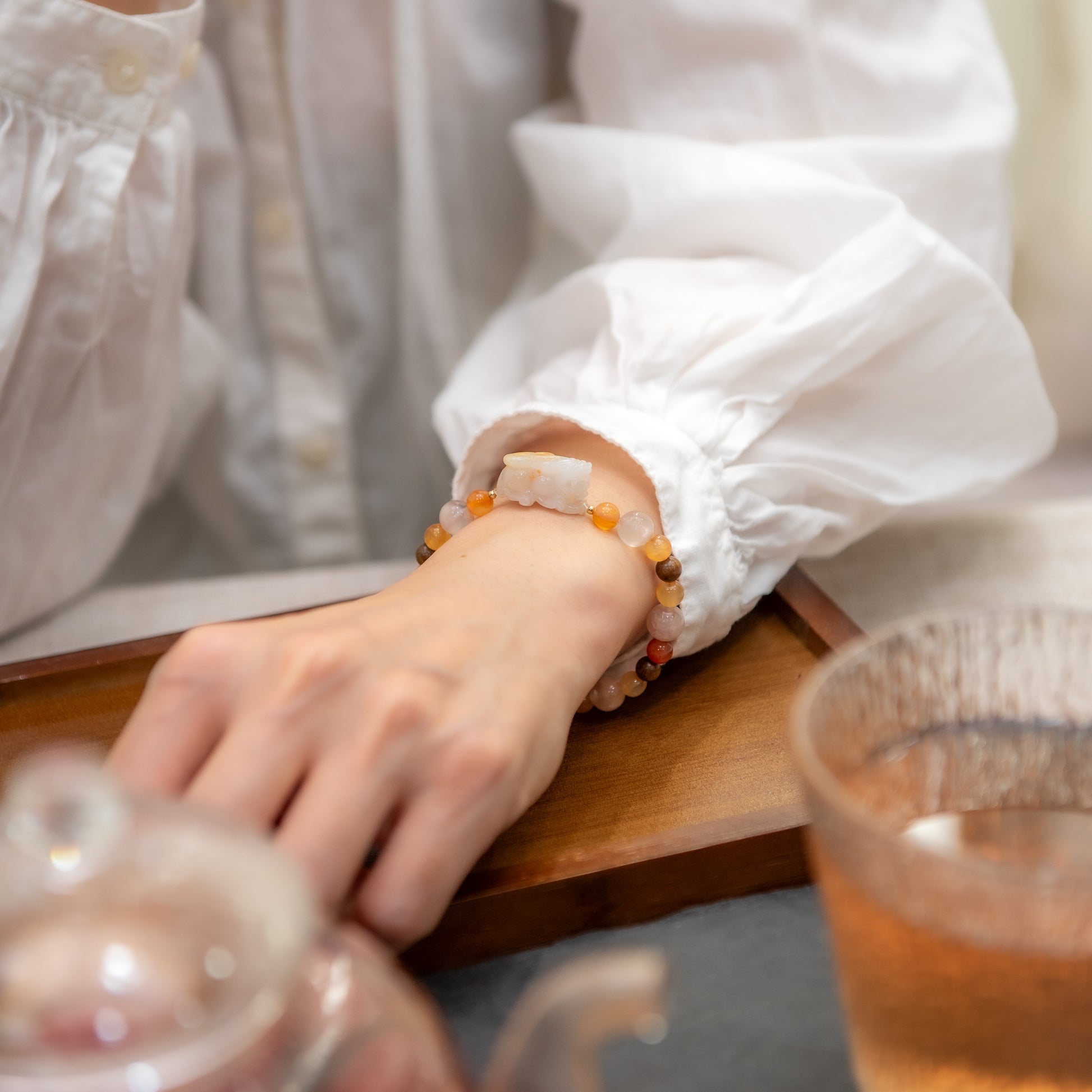 Person wearing a colorful bracelet on a wooden tray with a glass of tea.