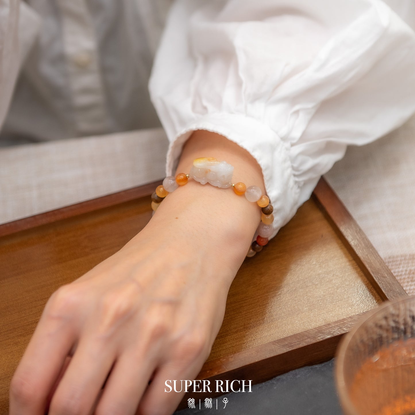 Person wearing a bracelet on a wooden surface with 'SUPER RICH' branding.